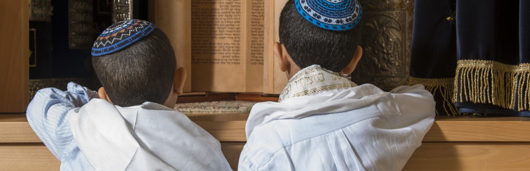 two boys standing in front of holy jewish scripts in a synagogue